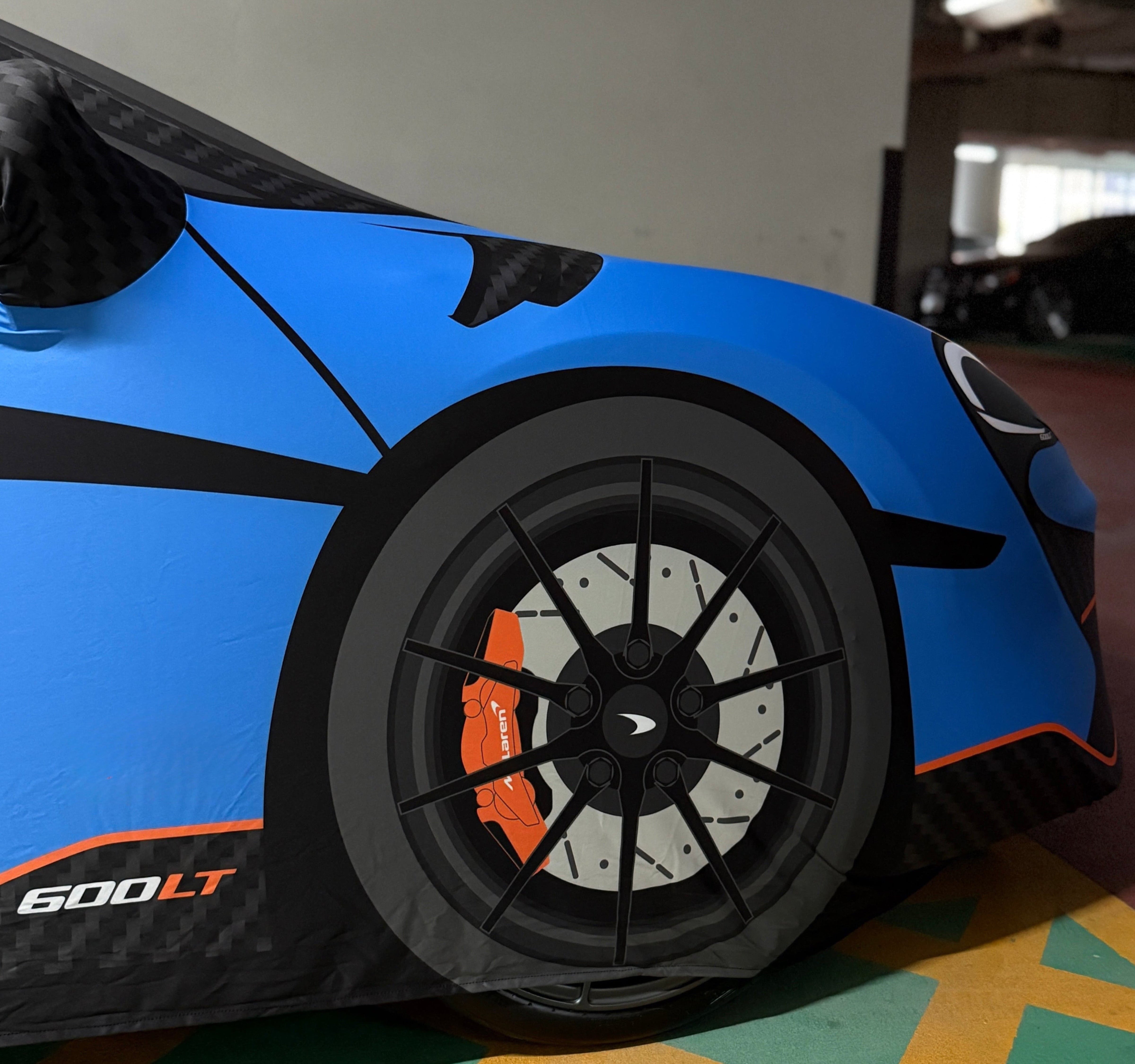 Close-up of a blue McLaren 600LT covered with a bespoke TyreDox indoor car cover, showing detailed wheel, brake calliper and aerodynamic lines — premium custom-fit protection for supercars.